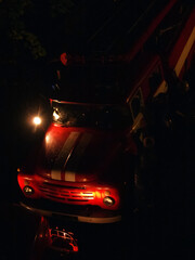 Firefighters. Preparing for the process of fulfilling duties. Fire service vehicles in the light of lanterns on a rainy night. Silhouettes of a firemen are visible near the car.