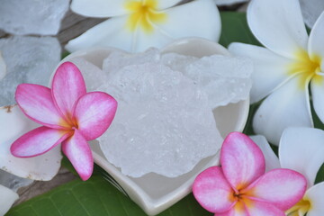 Alum cubes on ceramic pot and plumeria flowers background, concept for herb, bodycare, skincare, waterclear, spa, treatment, disease protection and protect armpit smell.	