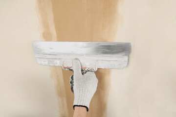 Worker plastering wall with putty knife indoors, closeup