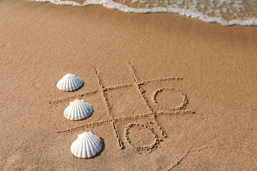Playing Tic tac toe game with shells on sand near sea, above view