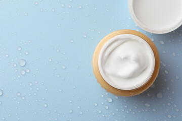 Jar of face cream on light blue surface covered with water drops, flat lay. Space for text