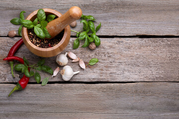Mortar with pestle and different spices on wooden table, above view. Space for text