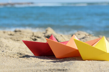 Three paper boats near sea on sunny day, closeup