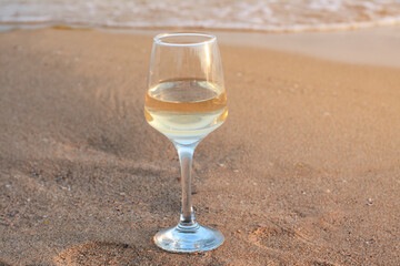Glass of tasty wine on sand near sea