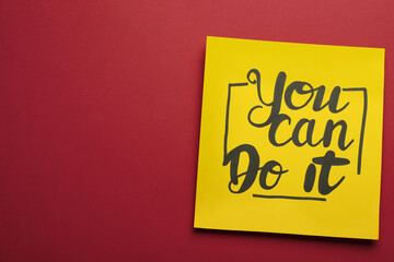 Yellow card with motivational phrase You Can Do It on burgundy background, top view. Space for text