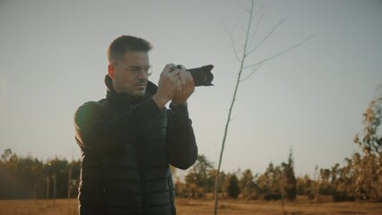 Medium slow motion of a young Caucasian male photographer, content creator, influencer, or travel blogger out in nature taking landscape photos at sunset. Generation Z millennial lifestyle concept.