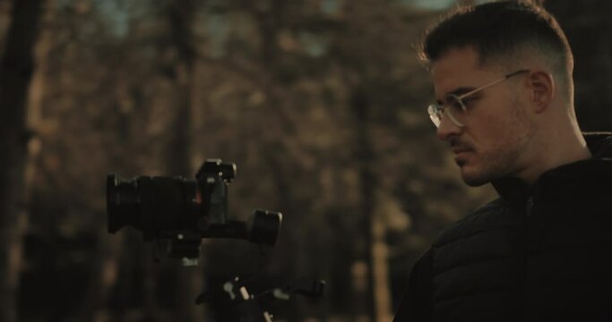 Inspiring millennial content creator balancing a motorized 3-axis electronic gimbal or steadicam out in nature at sunset. Videographer or filmmaker using a camera and stabilizer. Generation Z concept.