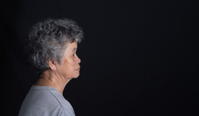 Side view of a senior woman looking away with a smile while standing on a black background