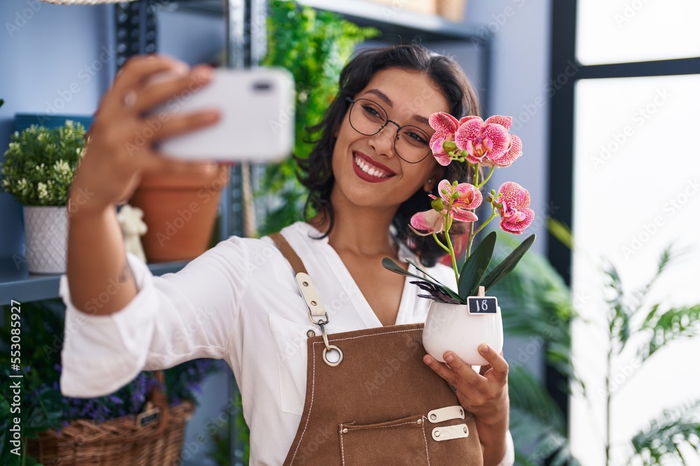 Sticker young beautiful hispanic woman florist make selfie by smartphone holding plant at flower shop