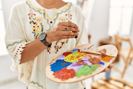 Young hispanic woman mixing color on palette at art studio