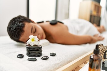 Obraz na płótnie Canvas Young hispanic woman having back massage using black hot stones at beauty center