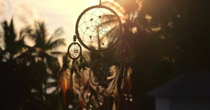 Close up silhouette of dreamcatcher with feathers flying in wind. Hunter of dreams against sunset. The concept of religion and mystical amulets 