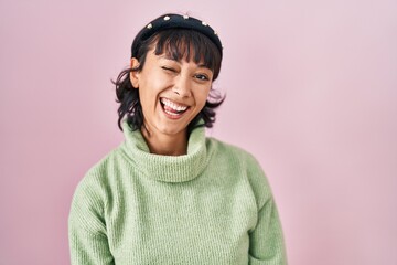 Young beautiful woman standing over pink background winking looking at the camera with sexy expression, cheerful and happy face.