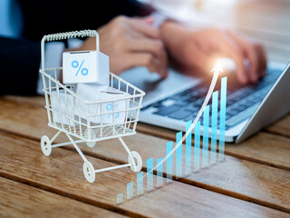 Online shopping purchase, sales increase, market trends concepts. Rising arrow on business growth graph near the shopping cart trolley with parcel boxes on desk near person using laptop computer. - obrazy, fototapety, plakaty