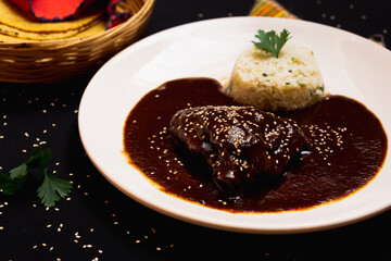 Delicious Mexican gourmet dish, mole with sesame chicken and rice on a black background.