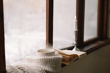 Fototapeta na wymiar Cozy winter still life. Cup of hot tea and an open book with a warm sweater on a vintage wooden windowsill. Cozy home concept. Sweet home.