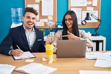 Young hispanic man and woman working at the office smiling happy pointing with hand and finger