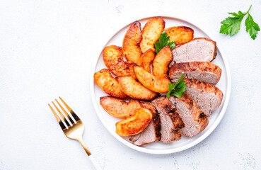 Baked pork tenderloin with quince or apple slices served on plate. White table background, top view