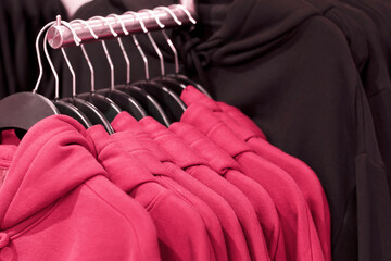 Hoodies on hangers in clothing store, concept of the color year 2023 Viva Magenta.
