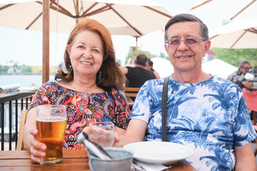 Senior hispanic couple drinking something cool, beer and water, at an outdoor table in a restaurant...