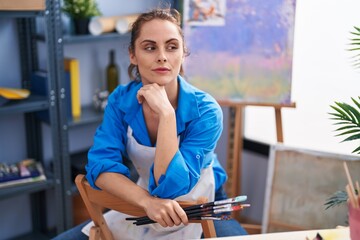Fototapeta premium Young woman artist sitting on chair with doubt expression at art studio