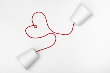 white cups phone and red string with heart shape