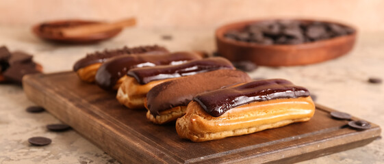 Wooden board with sweet eclairs on beige background