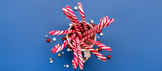 Cup with tasty candy canes on blue background, top view