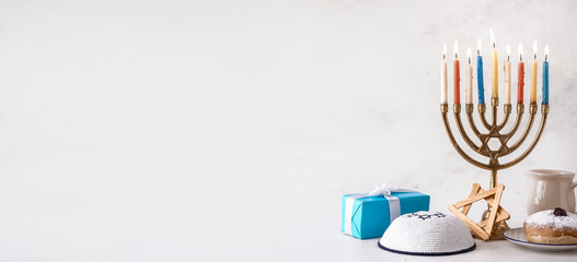 Menorah with glowing candles, Jewish hat and gift on light background with space for text. Hanukkah celebration