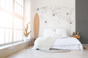 Interior of light bedroom with surfboard and printed world map on wall