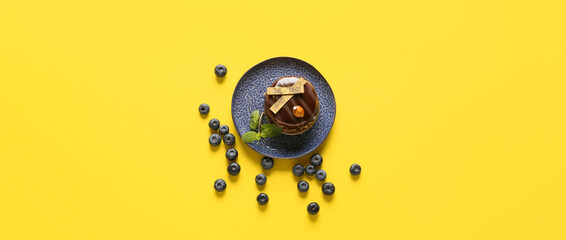 Plate with tasty chocolate cake and blueberries on yellow background