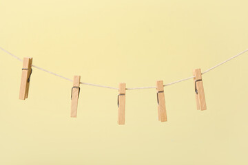 Wooden clothespins hanging on rope against color background