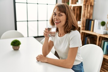 Young caucasian woman drinking water sitting on table at home