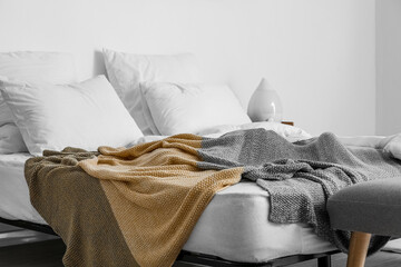 Comfortable bed with white pillows and blanket near light wall