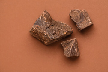 Pieces of delicious chocolate on brown background