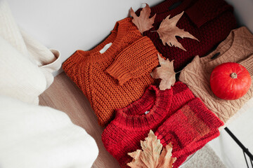 Obraz na płótnie Canvas Folded sweaters with autumn leaves and pumpkin on shelf in wardrobe