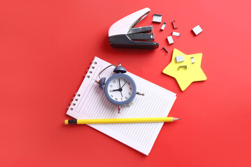 Set of stationery and alarm clock on red background