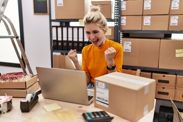 Young blonde woman working at small business ecommerce using laptop screaming proud, celebrating...