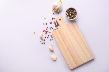 Obraz na płótnie Canvas Wooden cutting board, bowl of peppercorns and garlic on light background