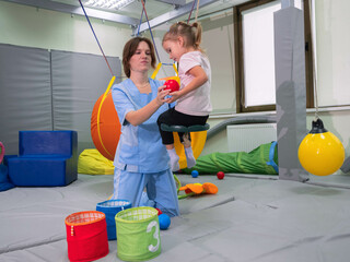 Child with physiotherapist on swing during sensory integration session. Little girl in...