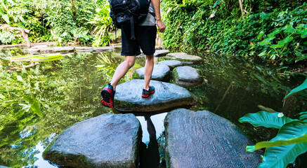 Male hiker with backpack crossing a river on stones