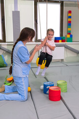 Child with physiotherapist on swing during sensory integration session. Little girl in...