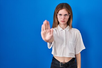 Beautiful woman standing over blue background doing stop sing with palm of the hand. warning expression with negative and serious gesture on the face.