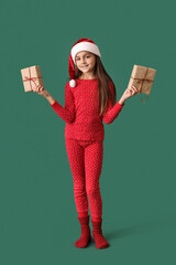 Little girl in pajamas with Christmas gifts on green background