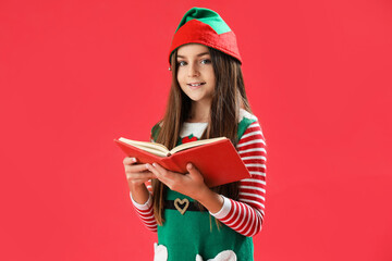 Little girl in elf pajamas with book on red background