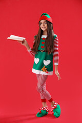 Little girl in elf pajamas with book on red background