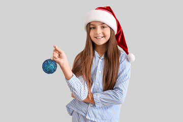 Little girl in pajamas with Christmas ball near light wall