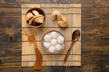 Fototapeta na wymiar Bamboo mat with bowl of tangyuan and fortune cookies on wooden background. Dongzhi Festival