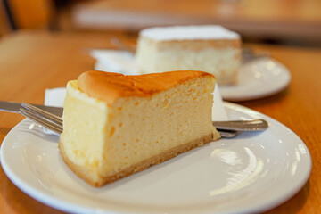Cheesecake on the plate with knife and fork in traditional European bakery shop background, selective focus