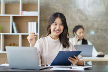 Fototapeta premium Attractive Asian businesswoman enjoying working using laptop at office. Looking at camera.
